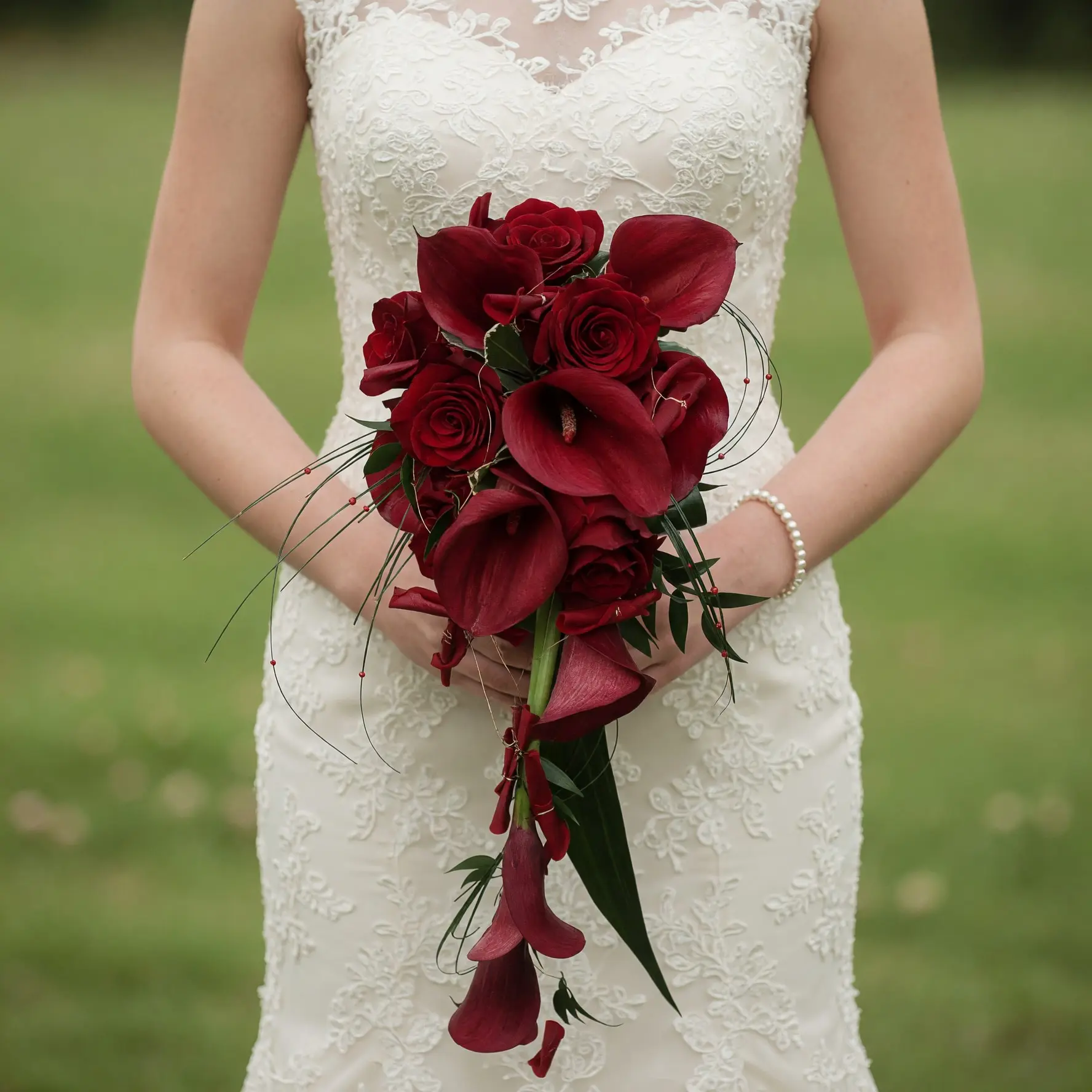 Burgundy wedding bouquet with deep red calla lilies, burgundy roses, dark greenery, curling grasses, and cascading flowers