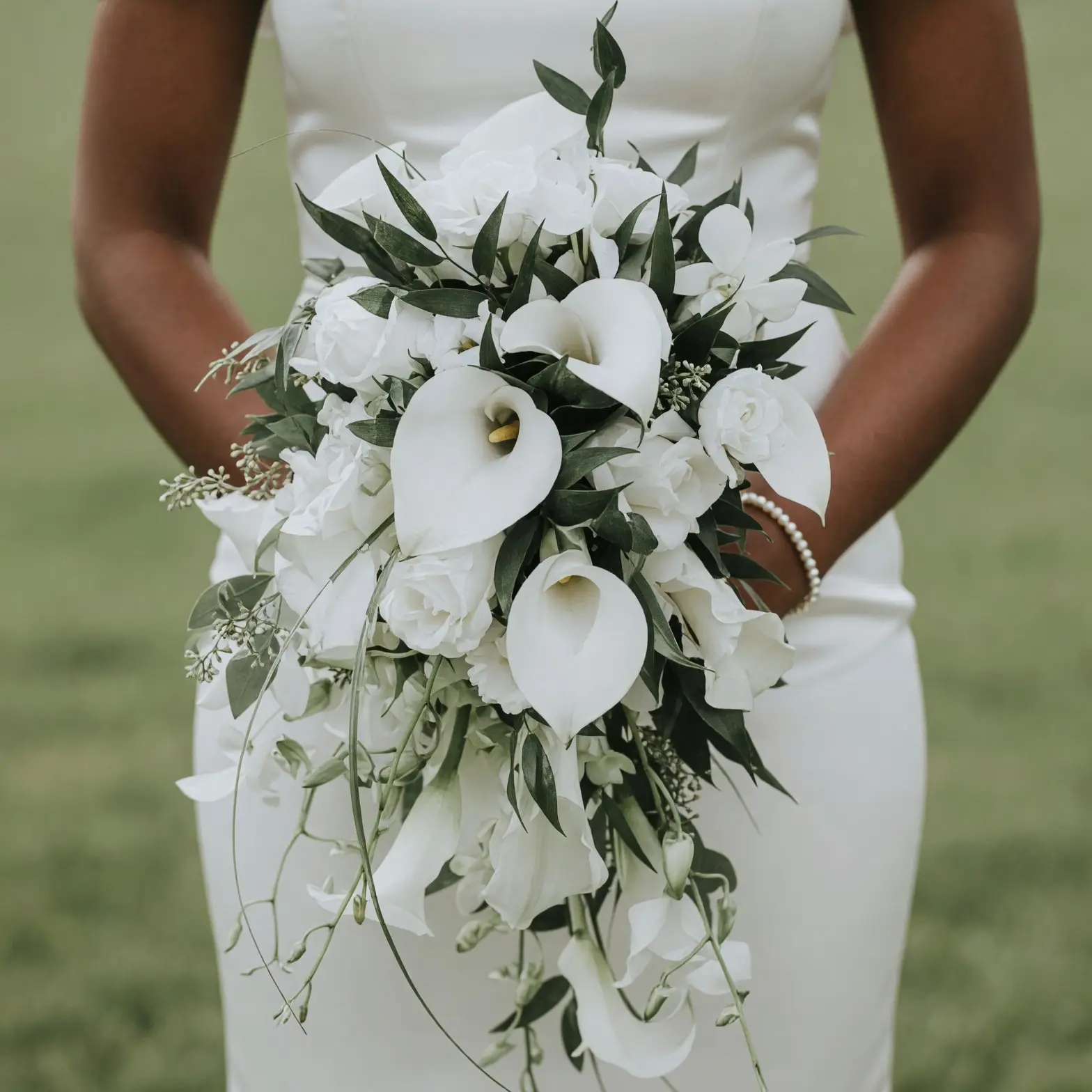 White calla lily wedding bouquet with white roses, orchids, trailing sweet peas, and dark green foliage in a cascading bridal design