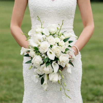 White calla lily and rose bouquet with ivory roses, delicate white blossoms, trailing flower stems, green buds, and fresh foliage