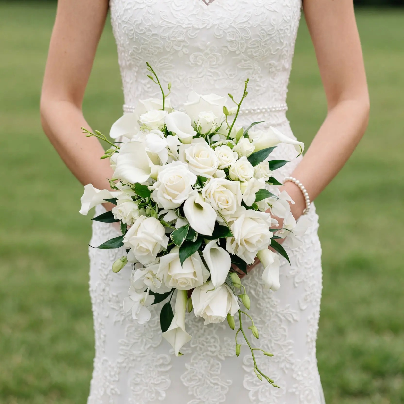 White calla lily and rose bouquet with ivory roses, delicate white blossoms, trailing flower stems, green buds, and fresh foliage