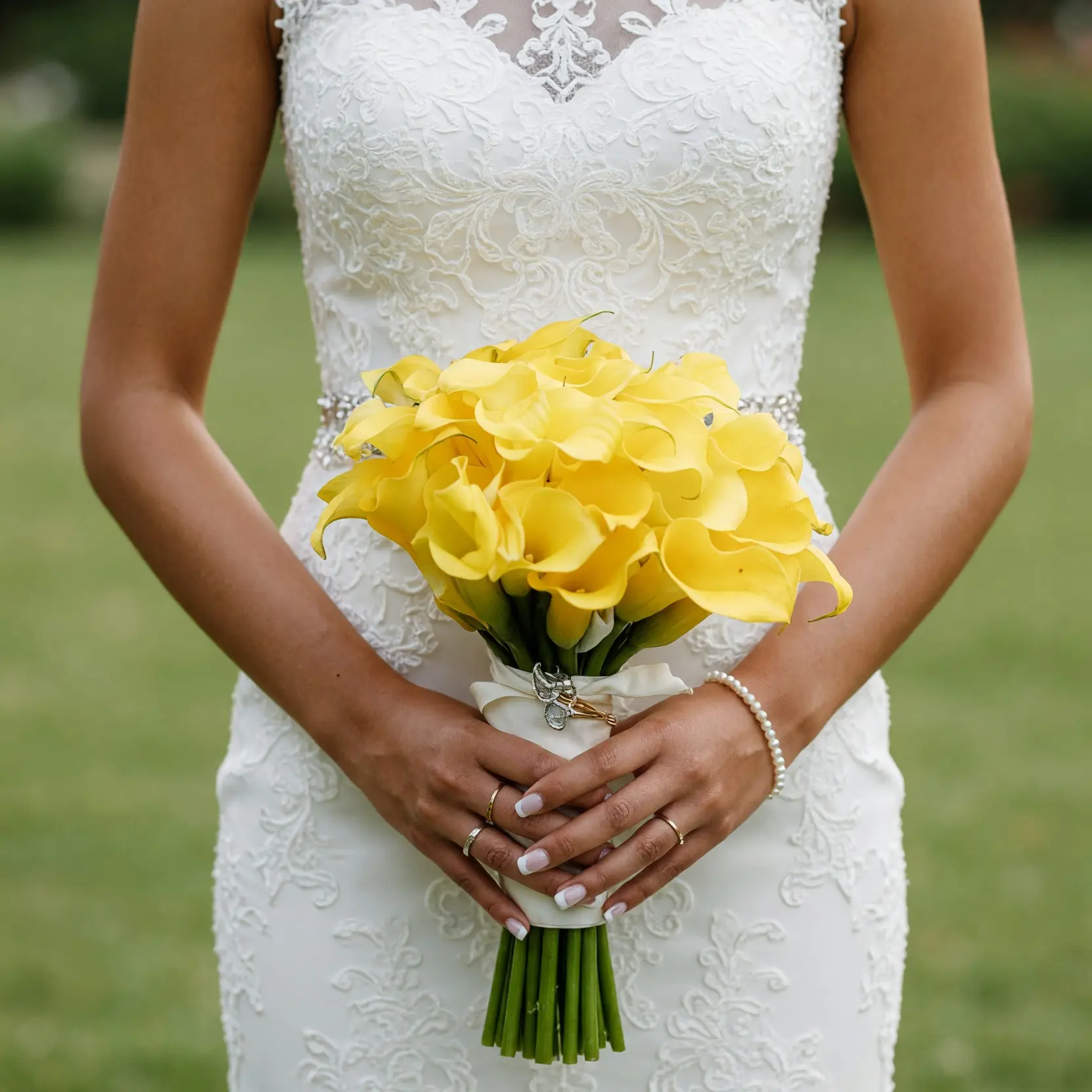 Yellow calla lily wedding bouquet with bright golden blooms, ivory ribbon wrap, long green stems, and a silver floral brooch