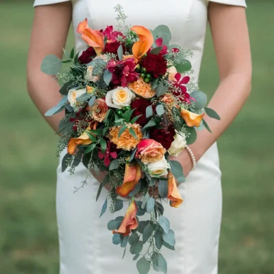 Bridal flowers bouquets with orange calla lilies, burgundy flowers, cream and peach roses, green berries, and cascading eucalyptus for a fall bride
