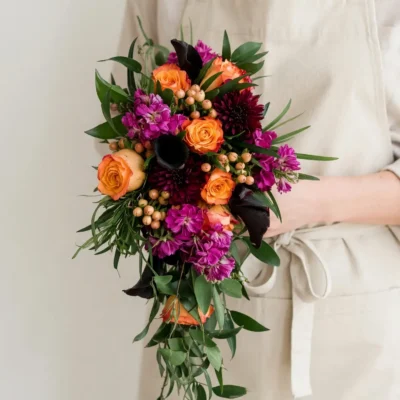 Bridal flowers bouquets with orange roses, fuchsia blooms, burgundy flowers, black calla lilies, peach berries, and cascading greenery for a fall bride