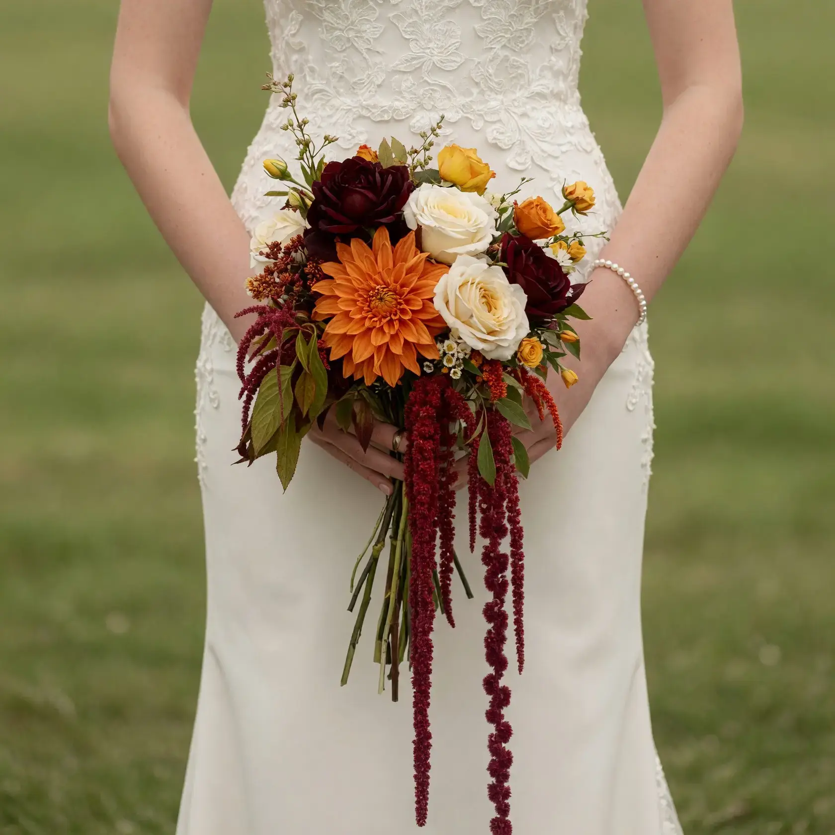Bridal blooms with burnt orange dahlia, burgundy roses, ivory roses, golden flowers, greenery, and trailing amaranthus for a fall bride