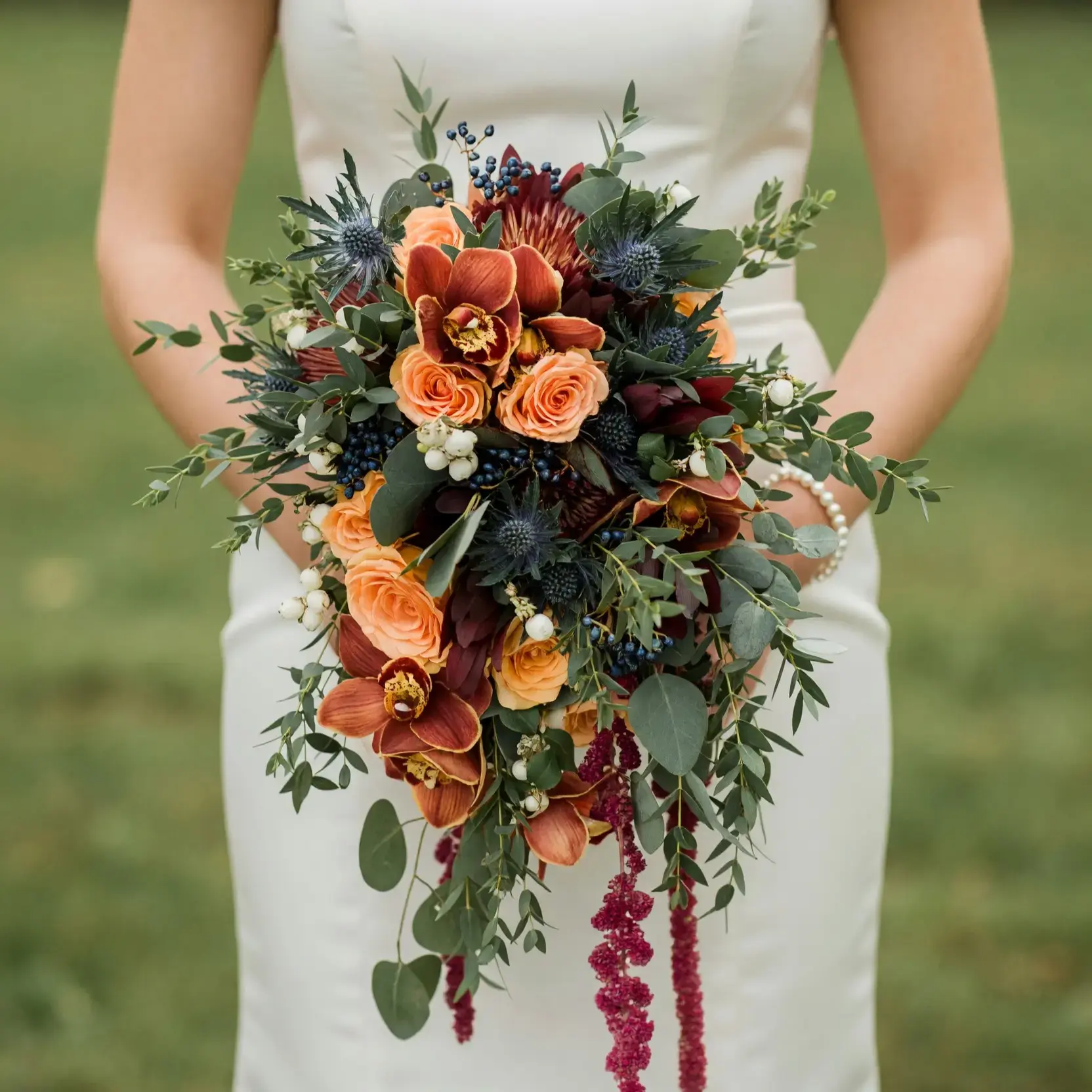Bridal blooms with copper orchids, peach roses, burgundy flowers, blue thistle, dark berries, eucalyptus, and cascading amaranthus for a fall bride