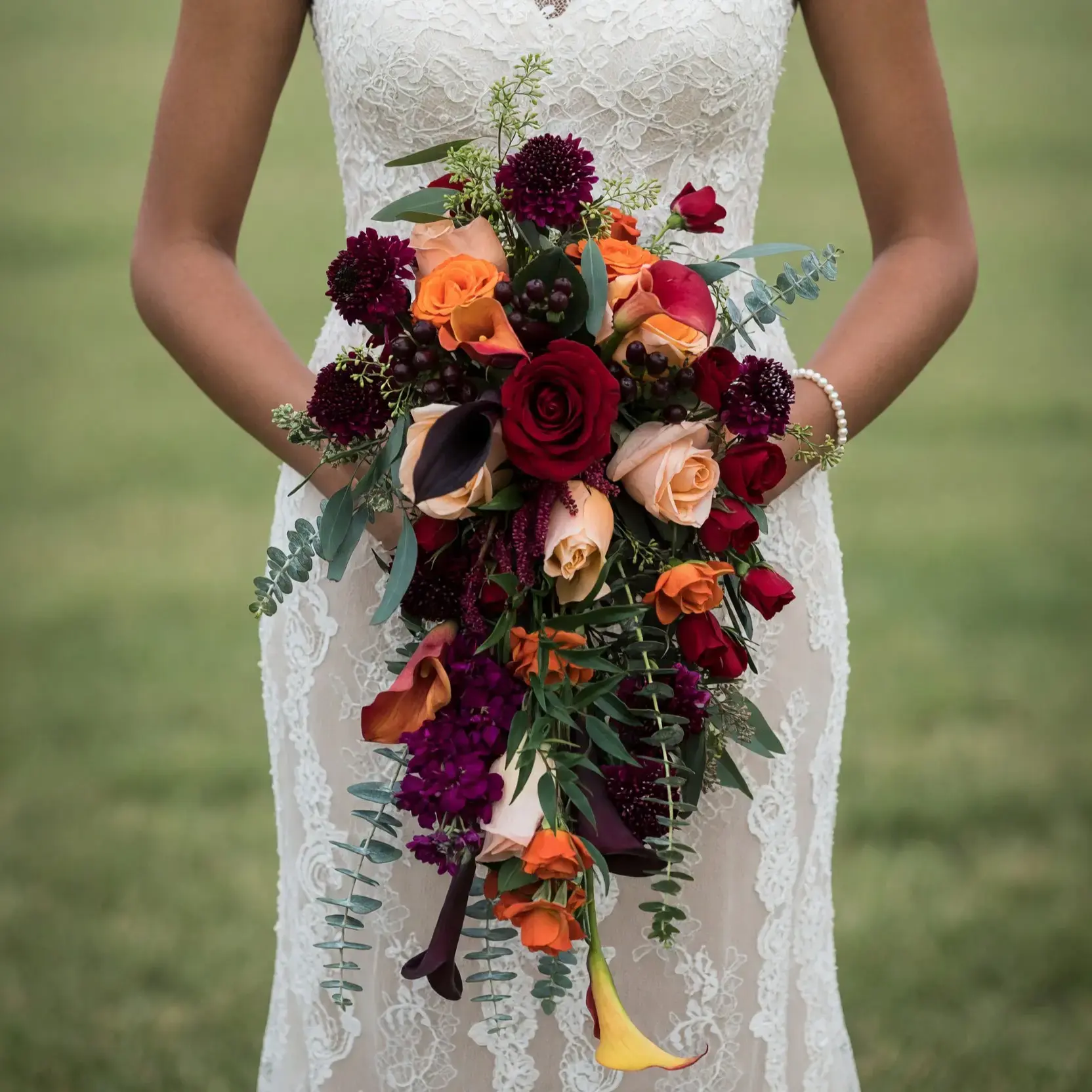 Popular wedding bouquets with burgundy roses, orange calla lilies, peach blooms, dark berries, chrysanthemums, and cascading eucalyptus for a fall bride