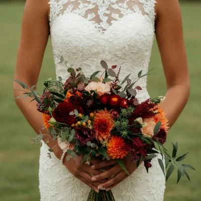 Bridal blooms with burgundy dahlias, burnt-orange chrysanthemums, peach flowers, berries, eucalyptus, and loose greenery for a fall bride