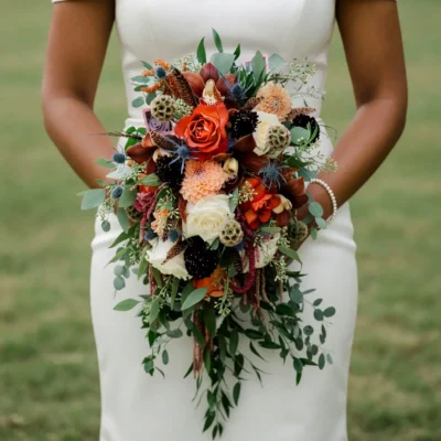 Bridal flowers bouquets with copper roses, brown orchids, ivory blooms, blue thistle, seed pods, eucalyptus, and cascading greenery for a fall bride