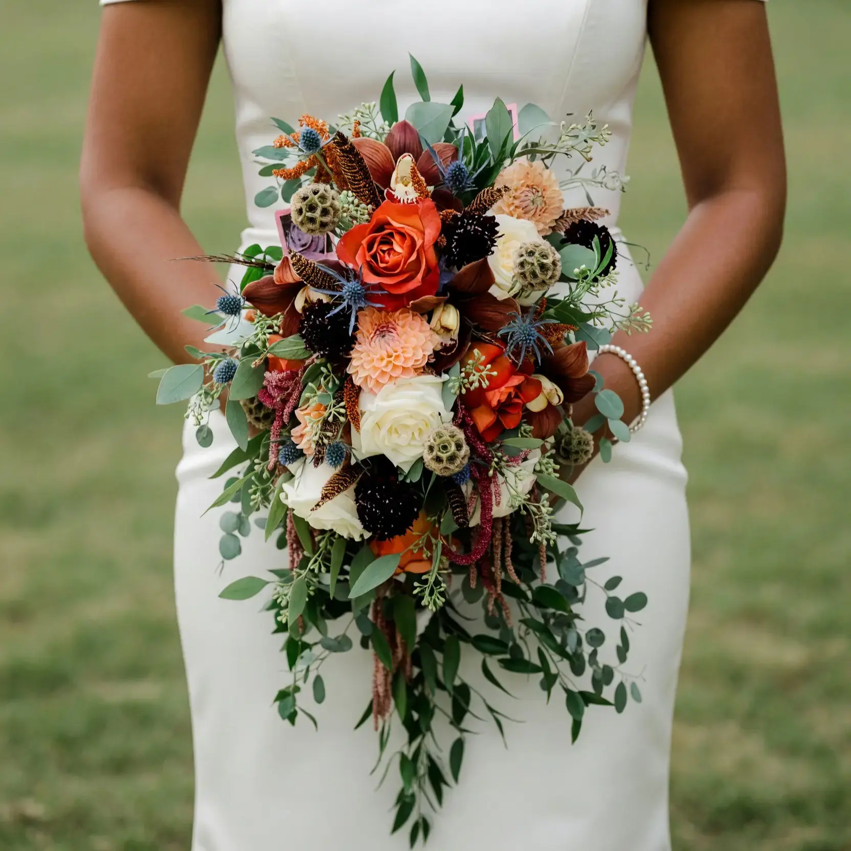 Bridal flowers bouquets with copper roses, brown orchids, ivory blooms, blue thistle, seed pods, eucalyptus, and cascading greenery for a fall bride