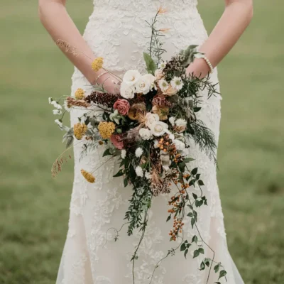 Boho style flowers with ivory roses, dusty blush blooms, golden flowers, orange berries, wild grasses, herbs, and cascading greenery for a fall bride
