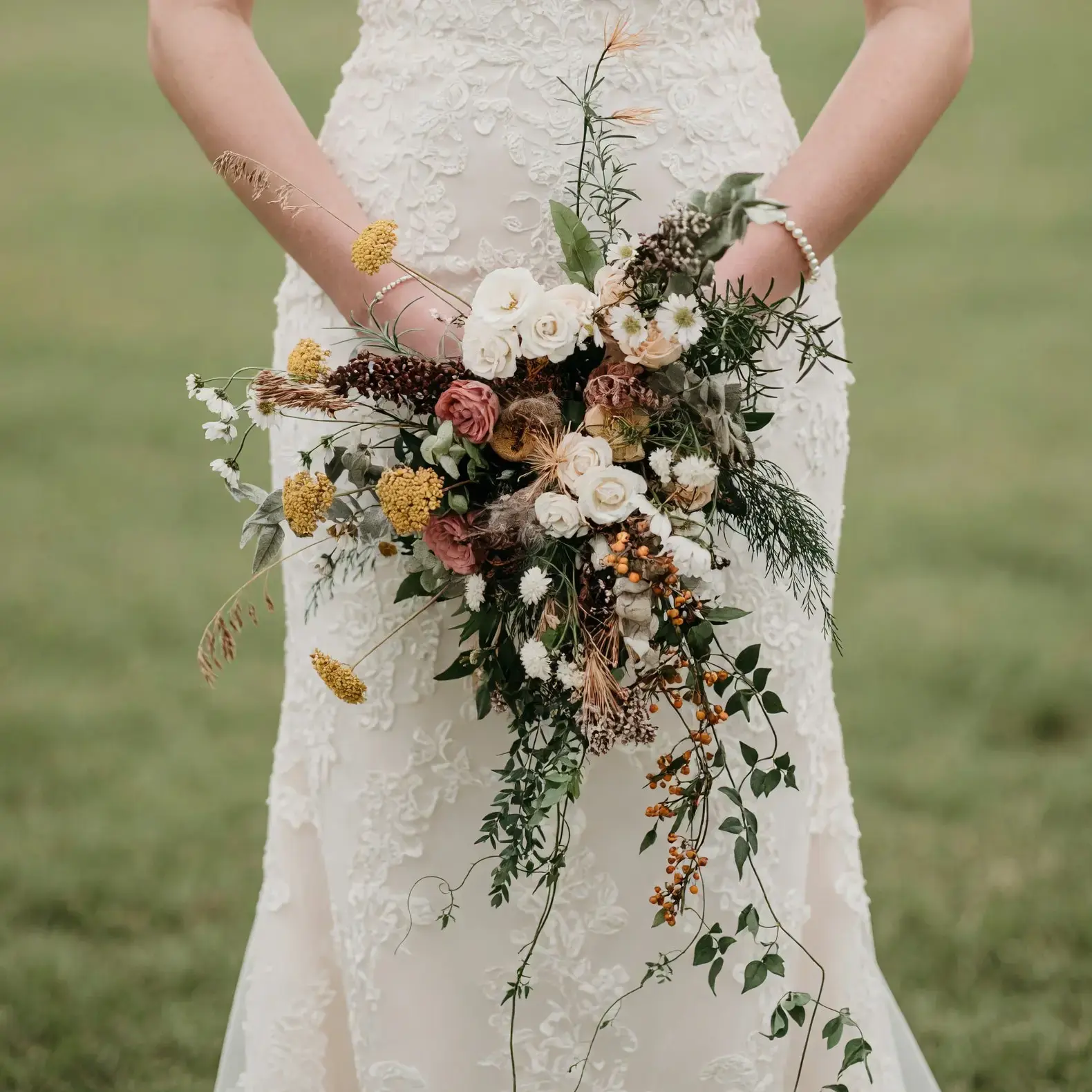 Boho style flowers with ivory roses, dusty blush blooms, golden flowers, orange berries, wild grasses, herbs, and cascading greenery for a fall bride