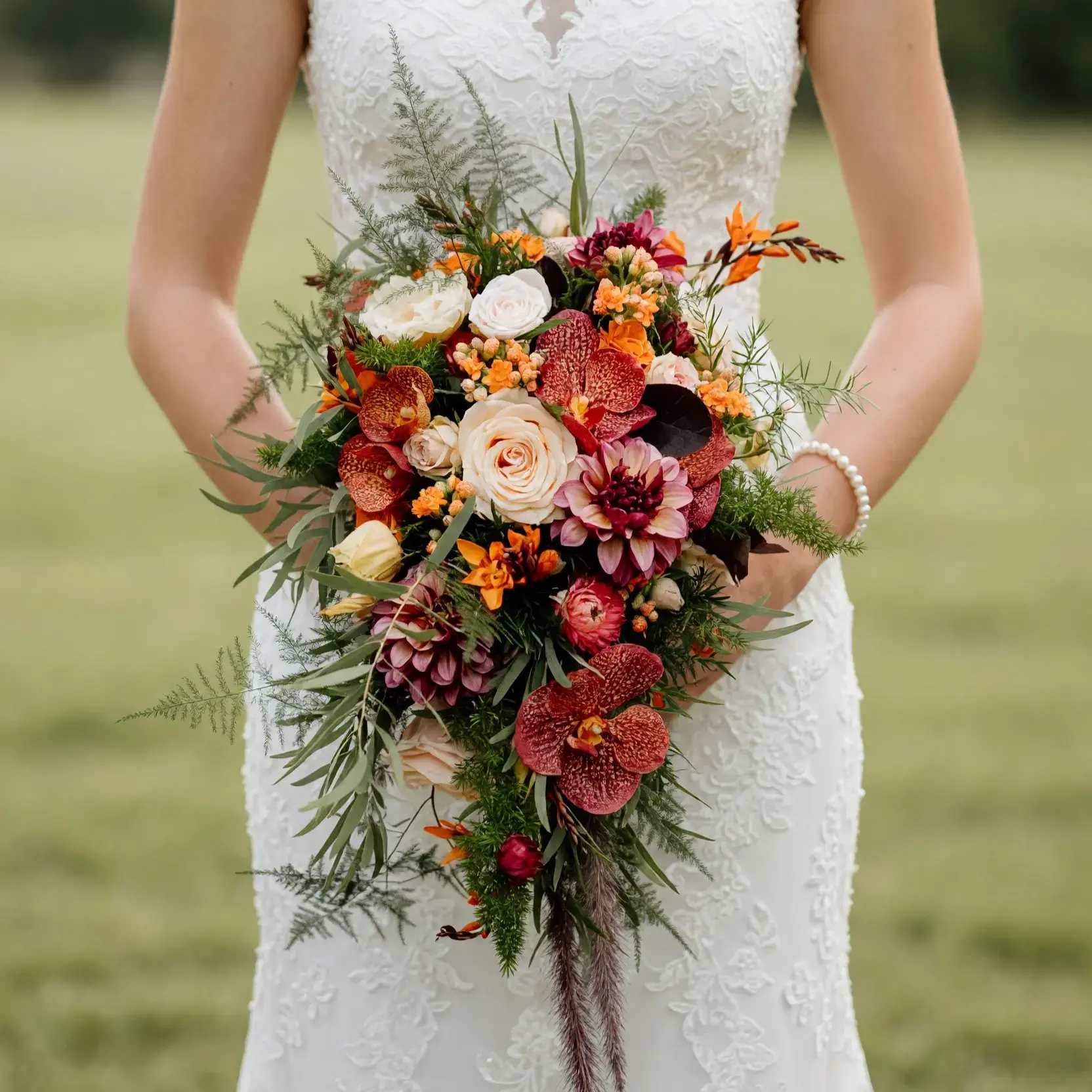 Bridal bouquet cost inspiration with rust orchids, ivory roses, burgundy chrysanthemums, orange flowers, and cascading greenery for a fall bride