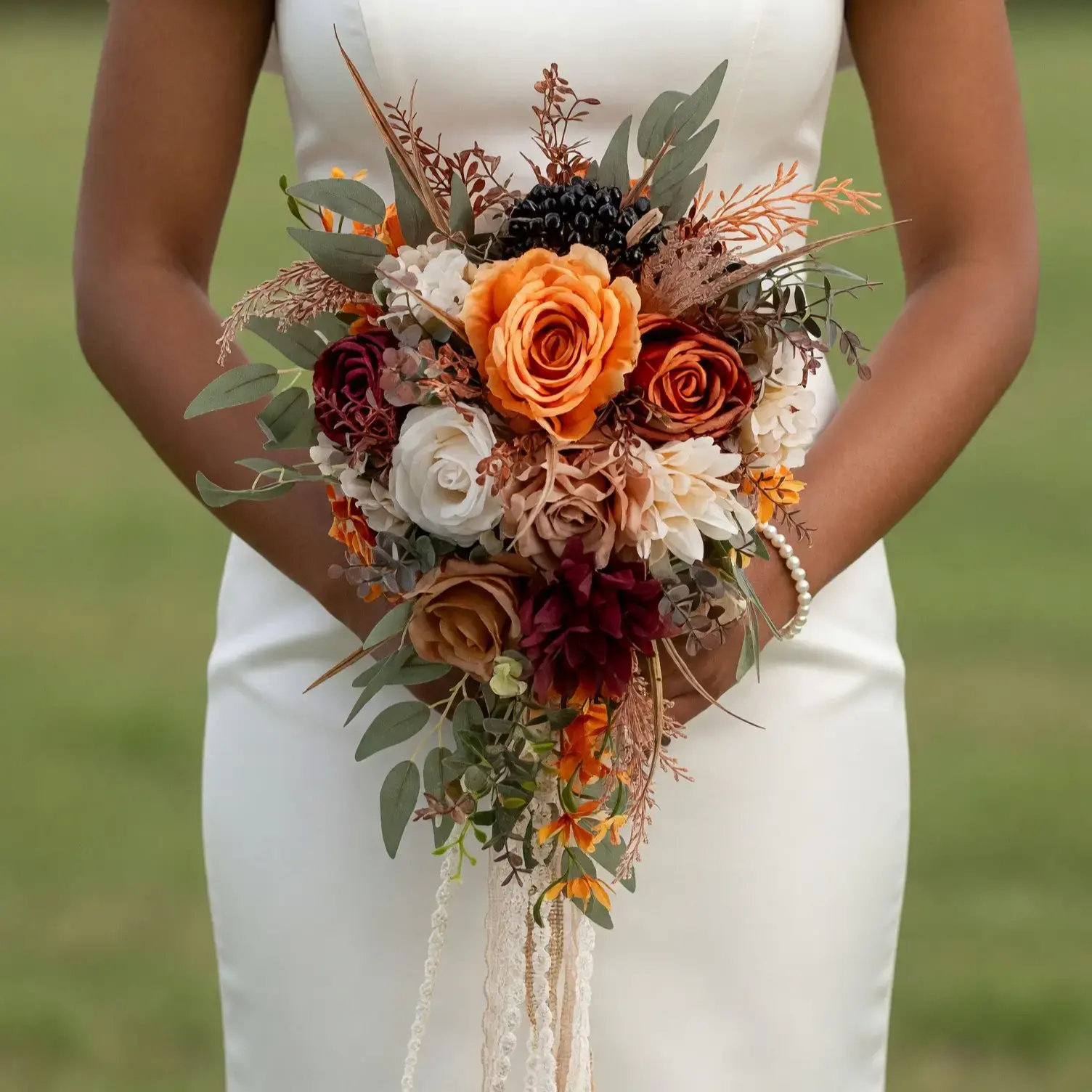 Fall bridal bouquet with burnt-orange and burgundy roses, ivory flowers, dark berries, eucalyptus, caramel blooms, and trailing cream lace