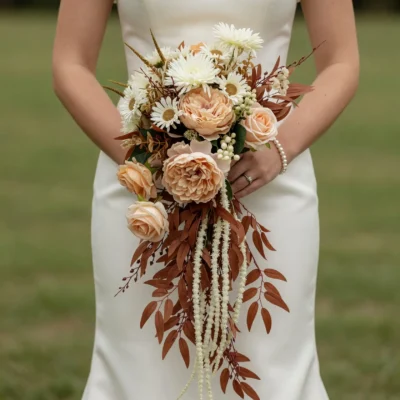 Popular wedding bouquets in boho style with peach roses, ivory daisies, rust foliage, pale berries, and cascading white flowers for an autumn bride.