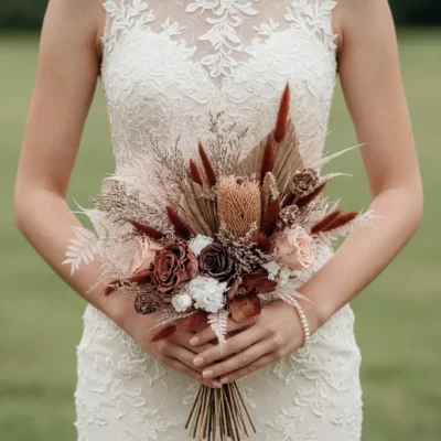 Boho bridal blooms bouquet with burgundy and blush roses, dried protea, rust bunny-tail grasses, preserved palm leaves, seed heads, and pale ferns.