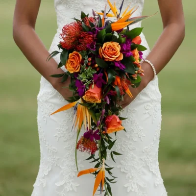 bridal blooms with orange roses bird of paradise red pincushion protea purple orchids and cascading tropical greenery