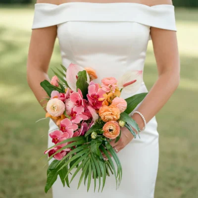 popular wedding bouquets with coral pink orchids peach ranunculus pale anthuriums orange tropical flowers and cascading palm foliage