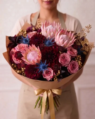 Luxury flowers Vancouver bouquet with pink protea, dusty pink roses, burgundy dahlias, blue accents and decorative gold details.