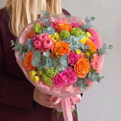 Colourful bouquet with orange roses, pink blooms, blue hydrangea, green accents, and eucalyptus wrapped in blush paper