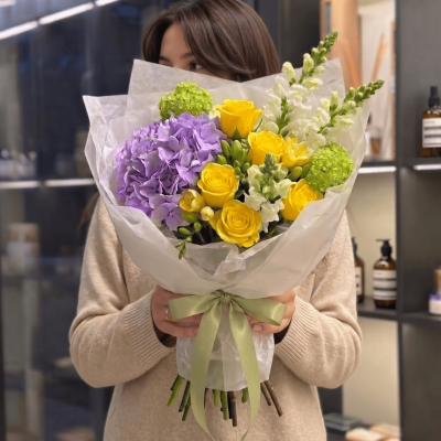 Yellow roses and lavender hydrangea bouquet with green accents wrapped in soft white paper