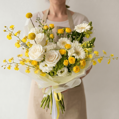 Elegant yellow and white bouquet with ivory roses, yellow spray roses, white gerbera-style flowers, and airy seasonal floral accents wrapped in soft ivory paper