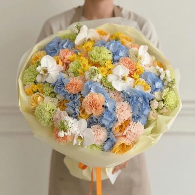 Luxury pastel bouquet with blue hydrangea, peach carnations, yellow roses, white orchids, and soft seasonal flowers wrapped in ivory paper